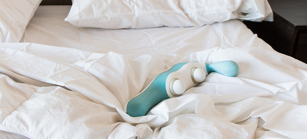 The hi massager lying on a crumpled comforter on a bed